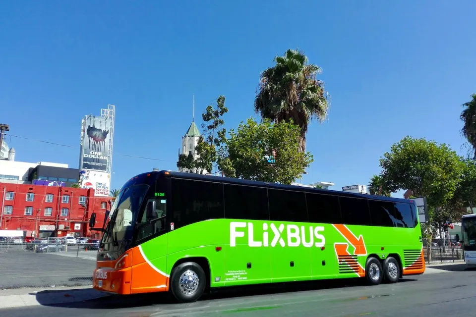Green Flixbus bus parked on street in Los Angeles, California with palm trees and Hollywood buildings in background on sunny day.